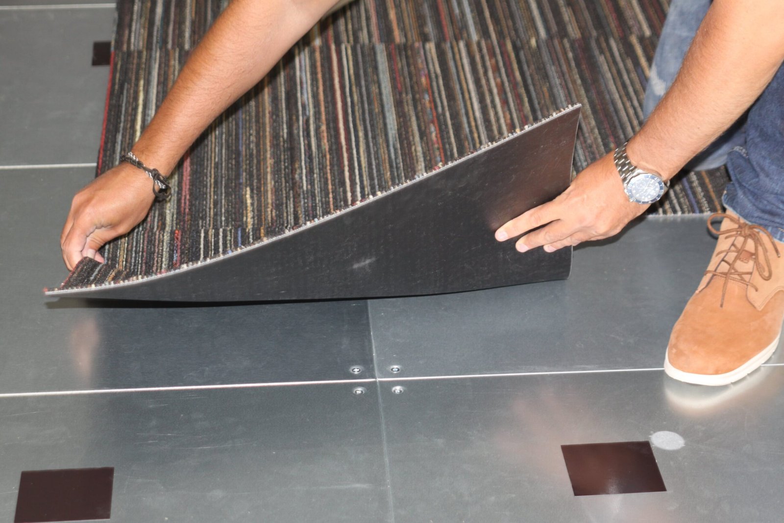 Silver metal floor with hands placing a brown carpet tile on top