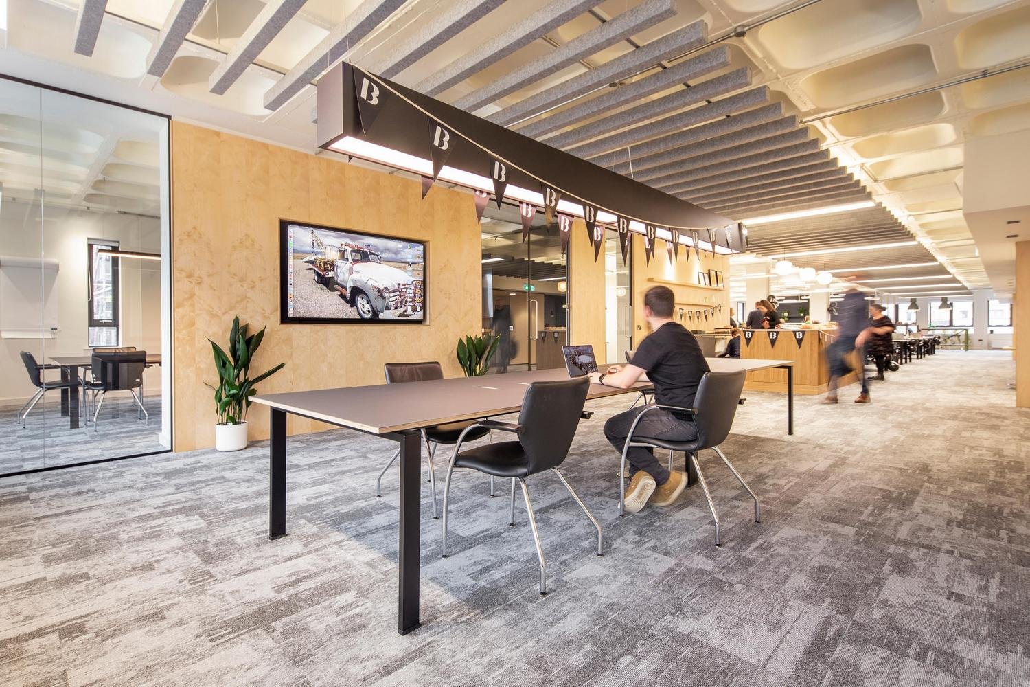 Office with grey carpet and a person working at a large table in front of a screeen